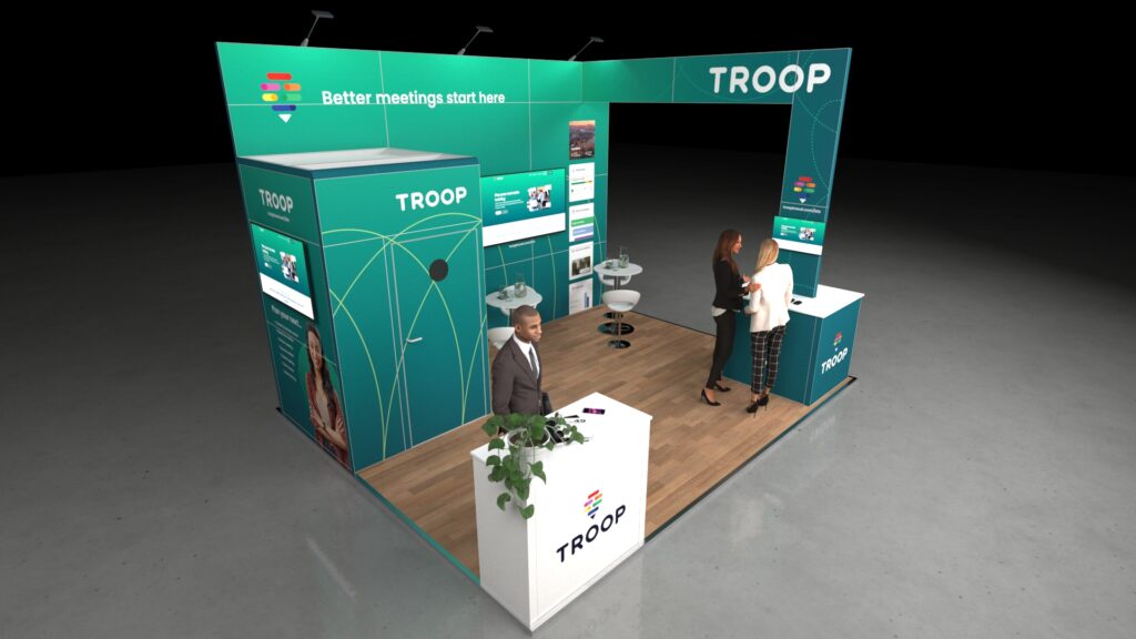 3D-rendered exhibition stand with a modern open layout featuring two counters, digital screens on the back wall, small tables with stools for meetings, and a person greeting visitors at the front desk on a wood-style floor